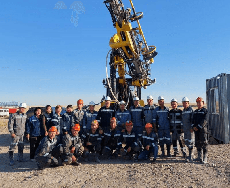 Field team assembled in front of a yellow drilling rig